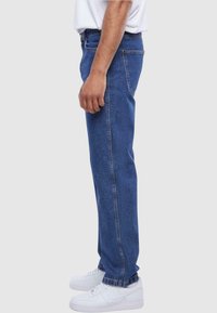 Blå denimjeans med rett snitt, middels høy livhøyde og synlig søm, kombinert med hvite sneakers.