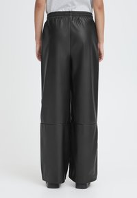 Pantaloni larghi in similpelle nera con vita elasticizzata, caratterizzati da una texture liscia e dettagli con cuciture, mostrati di schiena.