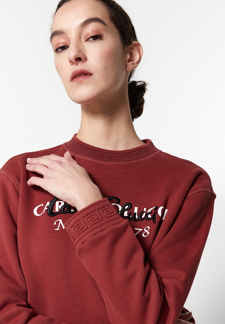 Bordeauxroter Pullover mit strukturiertem Kragen und Bündchen, mit weißer und schwarzer gestickter Schrift. Glattes Material, lockere Passform.