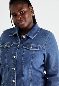 Τζάκετ από τζιν σε ανοιχτό μπλε με δομημένο σχέδιο, κλείσιμο με κουμπιά και δύο τσέπες στο στήθος. Διαθέτει κλασικό γιακά και απαλή υφή.