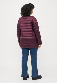 Burgundy puffer jacket with quilted design, shiny texture, and a mid-length cut, paired with blue flared jeans and black platform shoes.