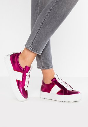 Osoba nosząca błyszczące magenta sneakersy z białymi paskami i grubymi białymi podeszwami, w połączeniu z szarymi, dopasowanymi jeansami.