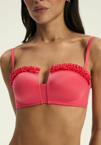 Korale różowy biustonosz z falbaniastymi krawędziami, formowanymi miseczkami i regulowanymi ramiączkami. Posiada głęboki dekolt w serek i gładką teksturę.