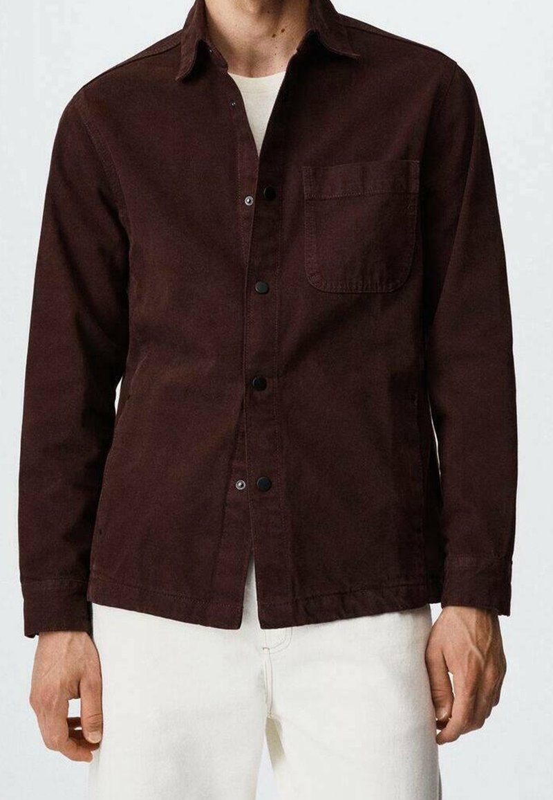 Camicia marrone con bottoni in un tessuto testurizzato, dotata di taschino sul petto, caratterizzata da bottoni neri e colletto.