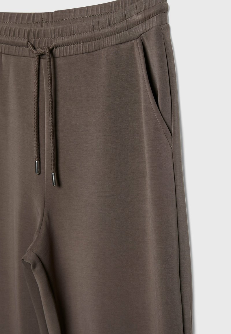 Braune Jogginghosen mit elastischem Bund, verstellbarem Kordelzug und seitlichen Taschen. Glatte Textur mit minimalistischem Design.