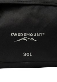 Zwarte stoffen tas met het "SWEDEMOUNT" logo en een berggrafiek. Capaciteit gemarkeerd als 30L. Tekst is in zilver op het oppervlak geperst.
