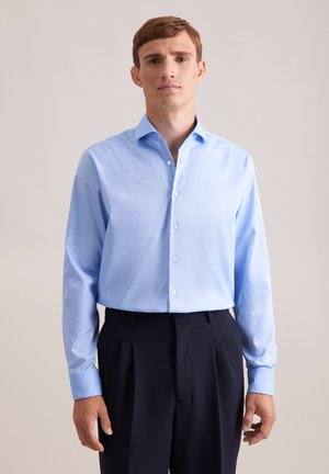 Chemise à manches longues bleu clair en coton, avec un col boutonné et une coupe ajustée. Associée à un pantalon plissé bleu marine.