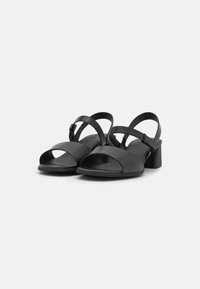 Black leather sandals with open toe and cut-out design. Features adjustable strap and block heel for stability. Smooth texture and minimalist style.