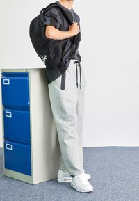 Svart ryggsäck med mesh-detaljer, grå sweatpants och vita sneakers. Överdelen är en mörk kortärmad tröja med grafik.