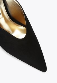 Scarpa nera in suede con tacco alto e punta affilata, caratterizzata da un interno dorato e un design a taglio aperto sul lato.