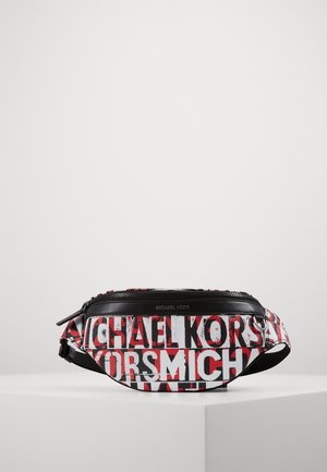 Banane Michael Kors noire, blanche et rouge avec fermeture éclair et sangle réglable sur un socle blanc.