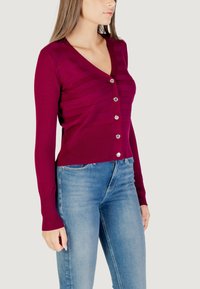 Cardigan fitted di un profondo color prugna con scollatura a V, motivo a righe verticali, cinque bottoni argentati e polsini a costine abbinato a jeans azzurri.