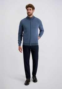 Blauer Zip-Pullover mit strukturiertem Kragen, kombiniert mit dunklen Hosen und braunen Schuhen. Der Pullover hat ein tailliertes Design und gerippte Akzente.