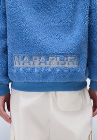 Blue fleece pullover with a textured surface, featuring a prominent embroidered logo in silver. Cuffs and hem are smooth, contrasting blue.