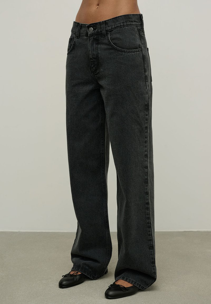 Aukštos juosmens juodos džinsinės kelnės su tiesiomis kojomis, turinčios priekinės kišenes, subtilius siūlus ir lygią tekstūrą.