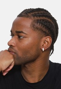 Boucle d'oreille en or et argent portée par une personne ayant des cheveux tressés. La boucle d'oreille présente une surface texturée avec une base lisse, mettant en valeur son design.