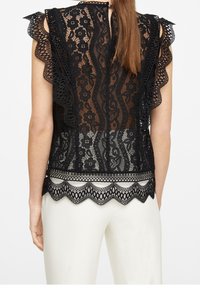 Haut en dentelle noire avec motifs floraux, manches à volants et bords festonnés. Le dos présente une fermeture goutte d'eau et un design en dentelle élaboré.