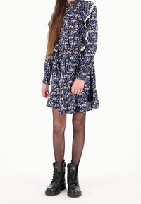 Abito floreale in blu navy con motivi bianchi e blu, spalle arricciate, orlo svasato, abbinato a stivali militari neri e collant a rete.