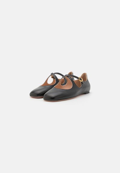 Zapatos de cuero negros con interior marrón, con diseños recortados y una doble correa con una hebilla dorada, suela plana.