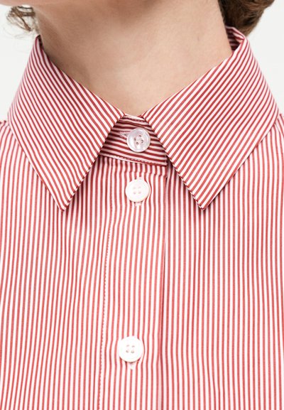 Κοντινό πλάνο ενός ατόμου που φοράει πουκάμισο με κόκκινες και λευκές κάθετες ρίγες, με κουμπιά και μυτερό γιακά.