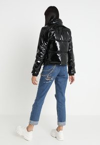 Czarna połyskująca kurtka puchowa z wysokim kołnierzem, pikowanym wzorem i krótkim krojem. Połączona z przetartymi niebieskimi dżinsami i białymi masywnymi sneakersami.