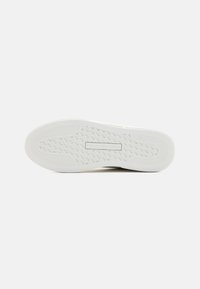 Gumová podešev bílého sneakeru s strukturovanými gripovými vzory a logo "Tommy Hilfiger" embosované uprostřed.