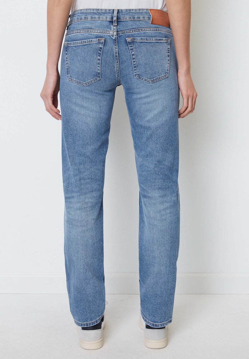 Helle blaue Denim-Jeans mit geradem Schnitt, fünf Taschen und einem braunen Lederpatch am hinteren Bund. Glatte Textur mit subtiler Ausbleichung.