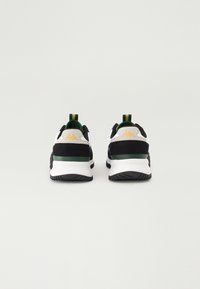 Zapatillas deportivas en blanco y negro con una franja de acento verde, tela texturizada y un logo amarillo en la parte trasera, que incluye un tirador.