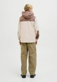 Veste beige clair avec des accents marron, capuche et poignets élastiques ; associée à un pantalon cargo vert olive. Design simple et fonctionnel.