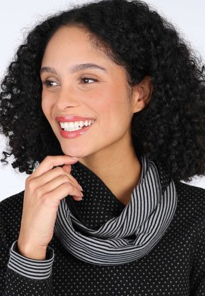 Black top with small white triangle patterns, featuring a striped cowl neck. Model touches her chin, showcasing a smooth texture and relaxed fit.