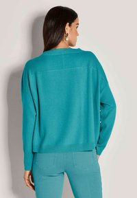 Türkisfarbener, übergroßer Strickpullover mit überschnittenen Schultern und gerippten Bündchen. Weiche Textur, minimale Nahtdetails und lockere Passform.