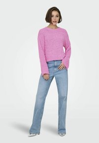 Maglione rosa testurizzato a maniche lunghe, abbinato a jeans svasati blu chiaro e tacchi silver. Finitura liscia e design casual.