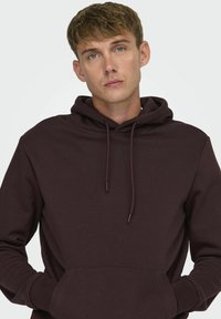 Sudadera con capucha burdeos en tejido suave, con un bolsillo canguro, capucha con cordones y puños acanalados. Diseño simple y limpio.