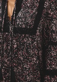 Top in tessuto nero con motivi floreali rosa, dettagli neri texturizzati, lacci con frange e scollatura a V profonda.