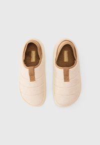 Beige slip-on bolyhos bélése Crocs, párnázott steppelt külső résszel és barna húzófülekkel a tetején, fehér háttér előtt bemutatva.