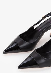Tacones slingback de cuero negro con una puntera de charol brillante y puntiaguda; presentan un diseño minimalista y un tacón de altura media.