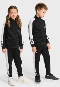 Czarno-białe dresy sportowe, z bluzą na zamek z fakturowanym górnym materiałem oraz spodniami w paski. Połączone z białymi i czarnymi sneakerami.