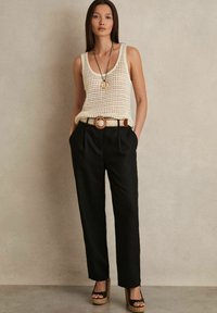 Canotta di maglia crema, pantaloni neri a vita alta con pieghe, cintura intrecciata marrone e sandali neri con zeppa e suola testurizzata.