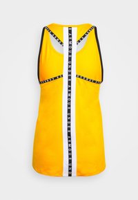 Gul atletlinne med racerback-design, svart kantband och en vertikal vit rand med upprepad text. Mjuk tygstruktur.