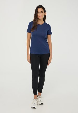 T-shirt navy a maniche corte realizzato in tessuto morbido, abbinato a leggings neri e sneakers bianche. La t-shirt ha un colletto rotondo e una vestibilità aderente.