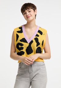Gul strikvest med sort leopardprint, V-udskæring og lys lilla ribbede krave. Korte ærmer og afslappet pasform. Grå denimjeans som nederdel.