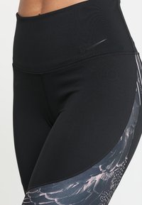 Ingrandimento di leggins neri a vita alta con un sottile logo Nike e pannelli laterali grigi a motivo piuma.