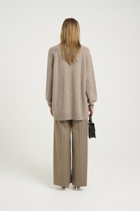 Beżowy oversize sweter z prążkowanymi mankietami, zestawiony z szerokimi beżowymi spodniami. Modelka trzyma małą czarną torebkę.