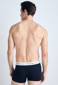 Sötétkék boxer alsó fehér derékkal, amelyen a TOMMY HILFIGER logó található. Simító anyag, szabott fazon és rövid szárhossz.