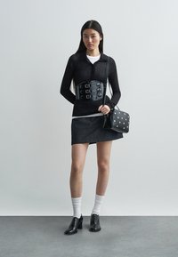 Musta pitkähihaisen paita, napillinen kaulus; musta keinonahkainen korsettivyö isoilla soljilla; tumma denimhame; musta laukku valkoisilla pilkuilla; mustat kengät.