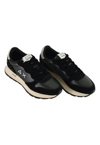 Schwarze Sneakers aus einer Mischung aus Wildleder und synthetischen Materialien. Sie verfügen über weiße Akzente, eine dicke, cremefarbene Sohle und ein Logo auf der Zunge.