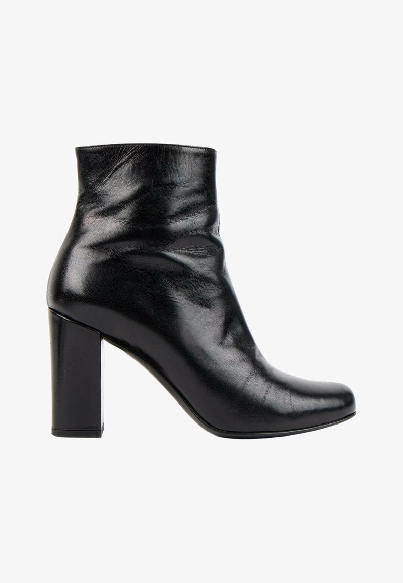 Bottine en cuir noir avec un bout arrondi, talon bloc et une texture lisse légèrement froissée sur fond blanc.