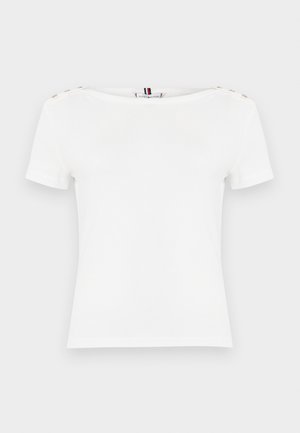 Haut blanc à manches courtes avec encolure bateau, avec des boutons décoratifs sur les deux épaules et une petite étiquette de marque au col arrière.