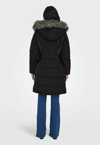 Svart puffjacka med avtagbar huva med pälsdetalj, quiltat mönster och sidodetaljer. Bärs över blå utsvängda jeans.