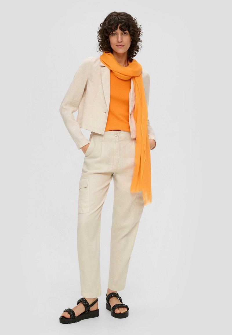 Leinenblazer in hellbeige, orange Oberteil, cremefarbene Cargo-Hose, orangefarbener Schal und schwarze Sandalen mit dicken Sohlen und geflochtenen Riemen.